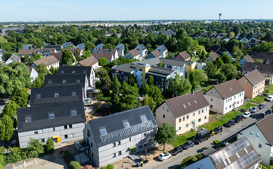 Aerial view of a suburban neighborhood with houses, some under construction, surrounded by trees and greenery on a sunny day.