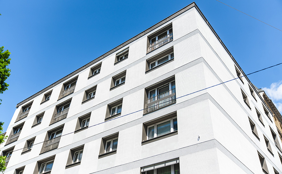 Corner view of a modern white apartment building with multiple windows against a clear blue sky.